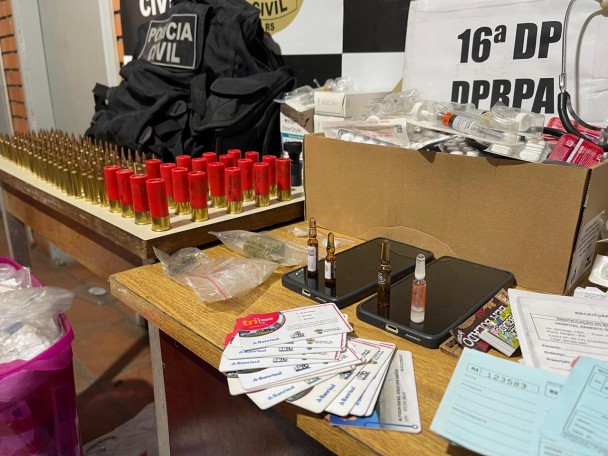 Materiais apreendidos expostos em mesa e ao chão com banner da Polícia Civil