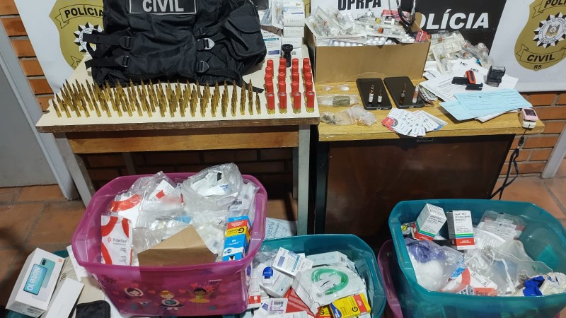 Materiais apreendidos expostos em mesa e ao chão com banner da Polícia Civil