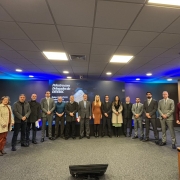 Participantes do encontro em pé posados para foto em frente ao banner do evento