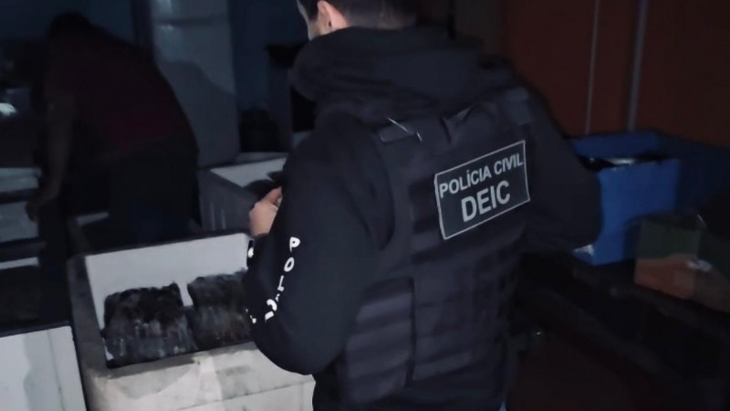 Policial civil com identificação de Polícia Civil DEIC fiscalizando caixa térmica branca