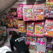 Policial civil abaixada com camiseta preta inscrito "polícia civil" verificando diversos brinquedos coloridos ao chão e pendurados em uma parede