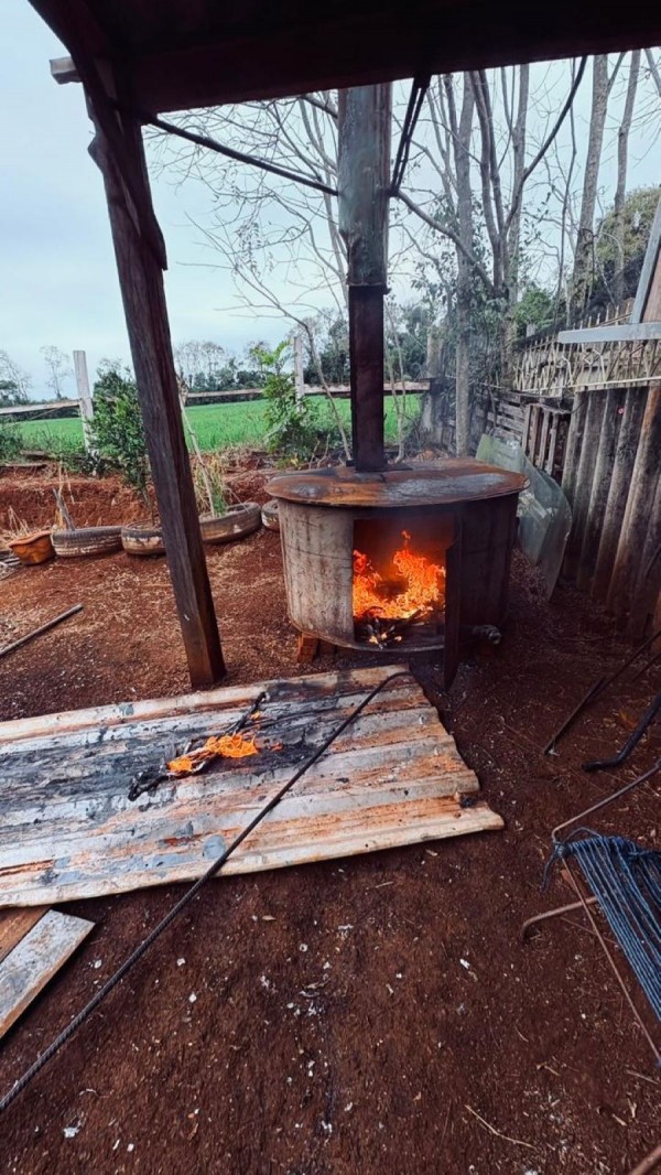 Forno com fogo cercado de materiais diversos como placas metálicas e madeiras em chão batido