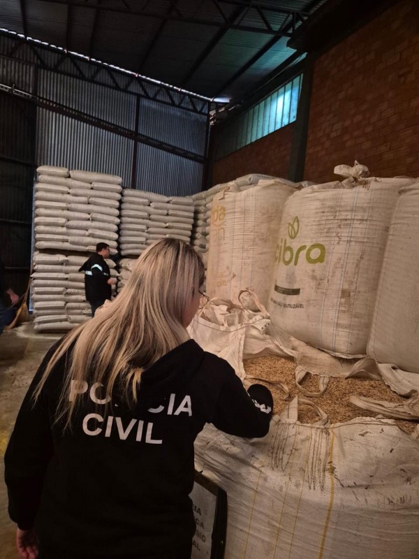 Policial civil mulher inspecionando bag com sementes e diversos sacos agrícolas em um grande galpão