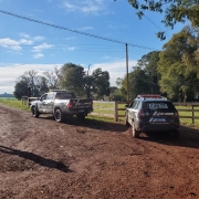 Viaturas ostensivas da Polícia Civil, com inscrições da DECRAB, paradas em uma estrada de chão batido em frente a uma porteira de fazenda