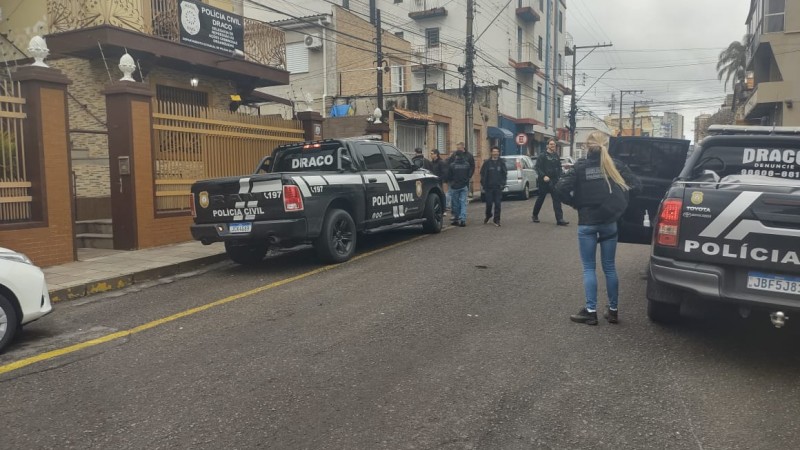 Veículos da Polícia Civil e policiais andando em rua em frente à Delegacia
