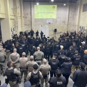 Policiais civis e militares em pé olhando projeção em parede sobre a operação