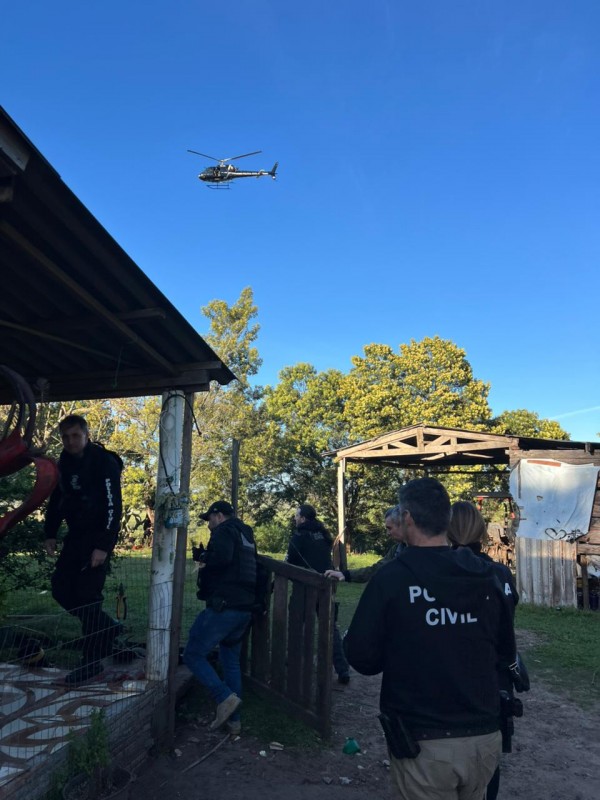Policiais civis adentrando em residência com helicóptero sobrevoando local