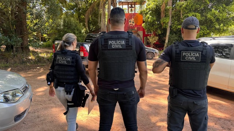 Três policiais de costas, sendo dois homens e mulher à esquerda, com coleta com a inscrita: Polícia Civil
