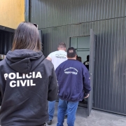 Agentes da Polícia Civil, Crea-RS, Corpo de Bombeiros e Prefeitura de Campo Bom de costas em fila entrando em uma porta de garagem grande e preta