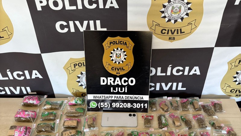 Papelotes de drogas embalados dispostas em cima de mesa, com logo e card da Polícia Civil ao fundo
