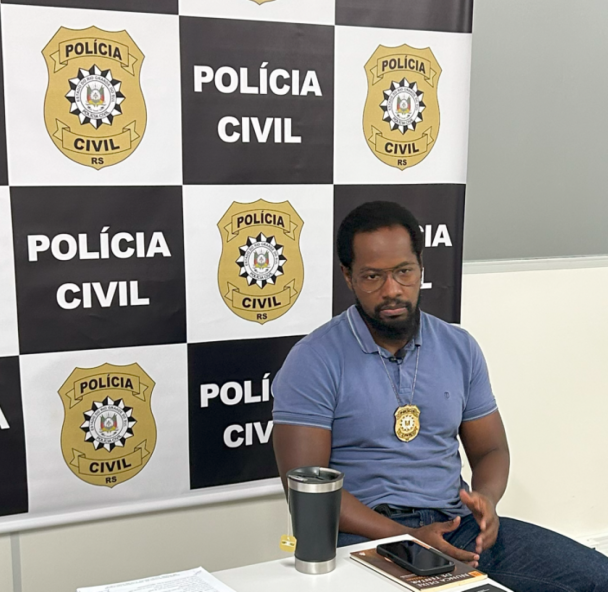 Homem negro à frente do banner da Polícia Civil