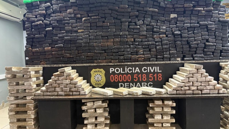Diversos tabletes de drogas de cores claras e escuras dispostos em cima de mesa com dizeres Pol&iacute;cia Civil e den&uacute;ncia 0800 518 518