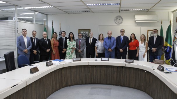 Pessoas em p&eacute; perfiladas lado a lado atr&aacute;s de uma mesa aredondada