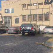 Viaturas policiais estacionadas em frente a um pr&eacute;dio de colora&ccedil;&atilde;o bege sede de Delegacia de Pol&iacute;cia