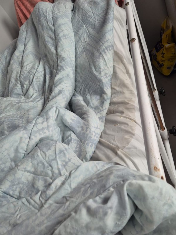 Cama mostrando cobertor e colchonete em estado ruim de conserva&ccedil;&atilde;o, com manchas e sujeira aparente